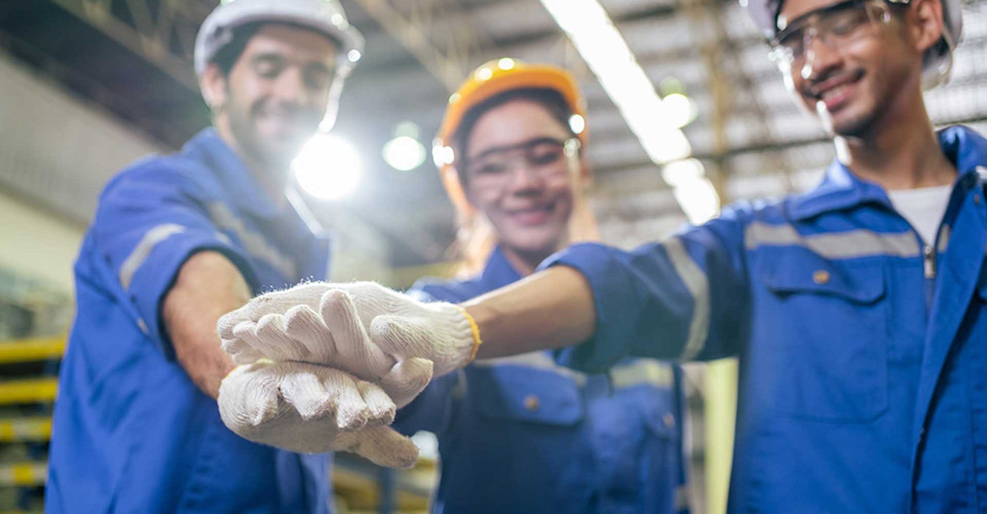 tre operai che sorridono e uniscono le mani perchè fanno parte di un team magazzinieri efficienti